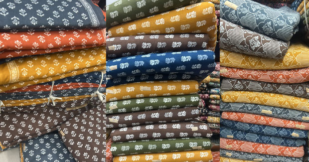 Stacks of folded Sanganeri print cotton fabric in mustard, orange, navy and olive with small floral motifs