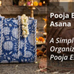 Blue floral printed Jaipur cotton pooja bag with asana, placed beside a diya and marigolds at a temple altar